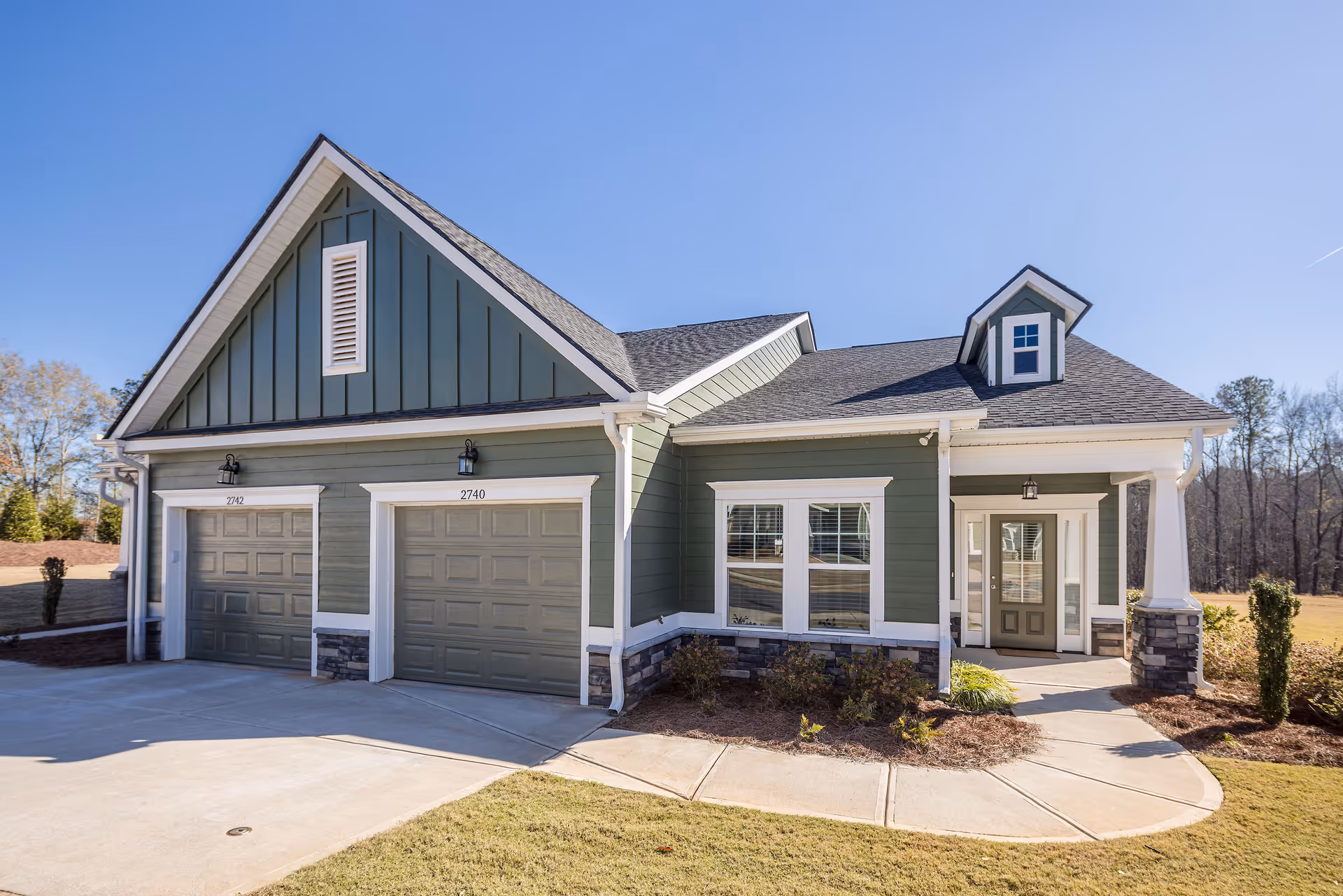 Green modern senior living facility exterior with two garage bays and a front entrance.