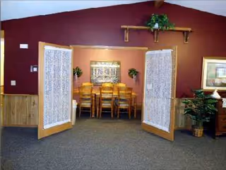 Double doors with lace curtains open to a wooden dining table inside a burgundy-walled dining room.
