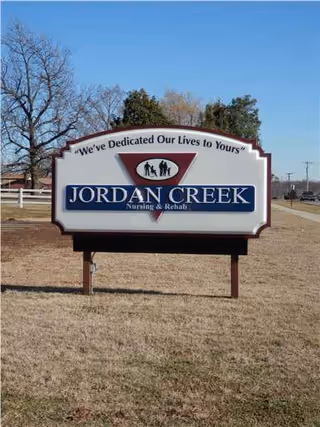 Outdoor sign reading Jordan Creek Nursing and Rehab on a grassy lawn under blue sky.