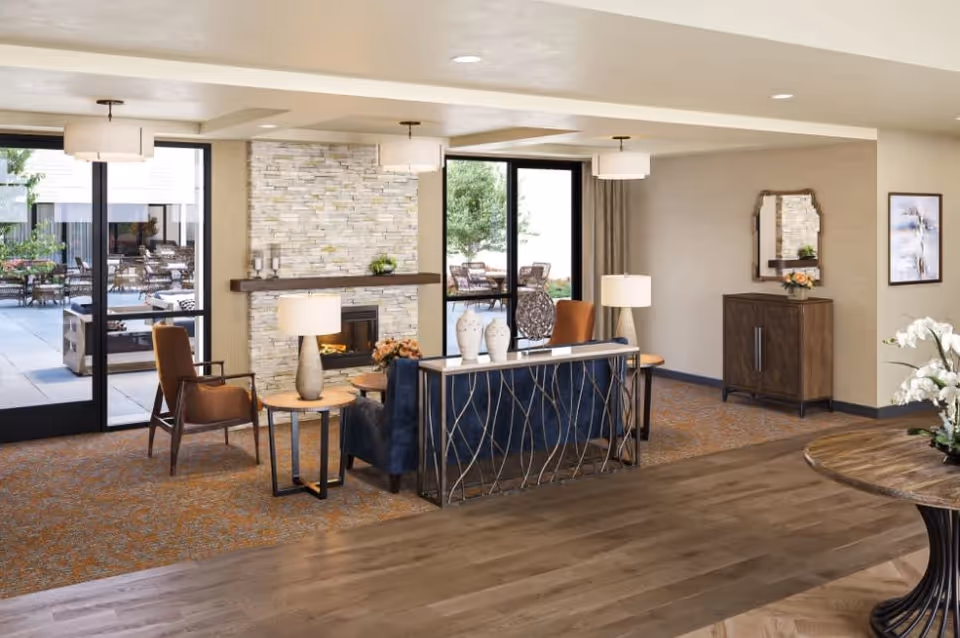 Bright communal lounge with seating, a stone fireplace, and glass doors opening to an outdoor patio.