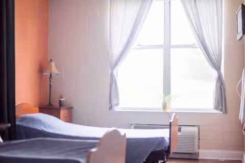 A patient room with two beds, a window, and a nightstand.