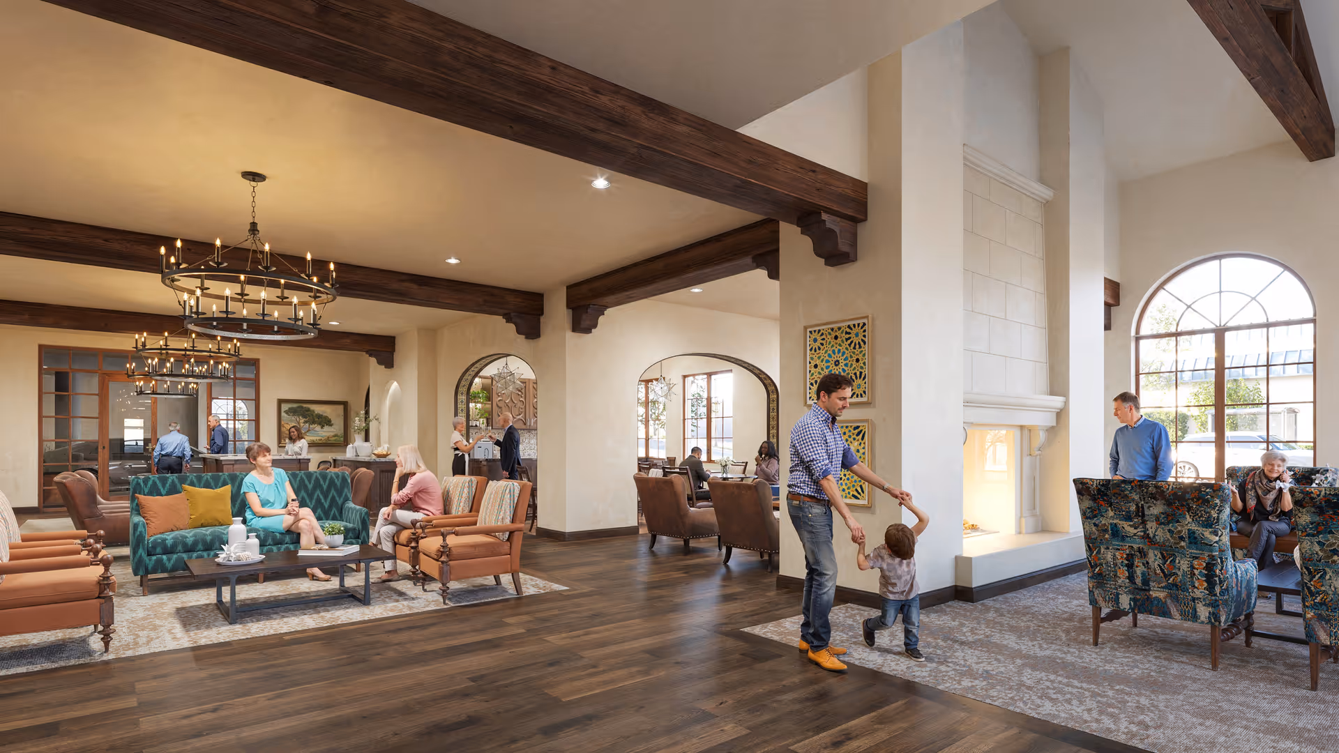 A spacious and warmly decorated living room area in a senior living facility with wooden beams on the ceiling, large windows, and a fireplace. Several groups of people are seated on sofas and armchairs engaged in conversation, while a man plays with a young child near the fireplace. The room features patterned rugs, chandeliers, and decorative wall art.