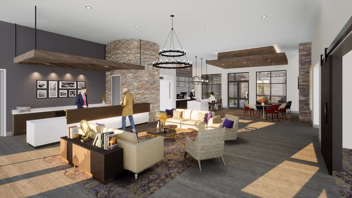 A spacious senior living facility common area with a reception desk where two people are interacting. The room features modern furniture including sofas, armchairs, a coffee table, and a bookshelf with books and decorative items. There is a stone accent wall behind the reception desk and large windows letting in natural light. In the background, there is a dining area with tables and chairs, and a kitchen or service counter with staff. The flooring is wood, and the ceiling has recessed lighting and decorative wooden panels.