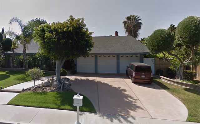 Front exterior view of a single-story residential building with a three-car garage, a driveway with a parked maroon van, well-maintained green lawn, trimmed trees, and a white mailbox at the curb.