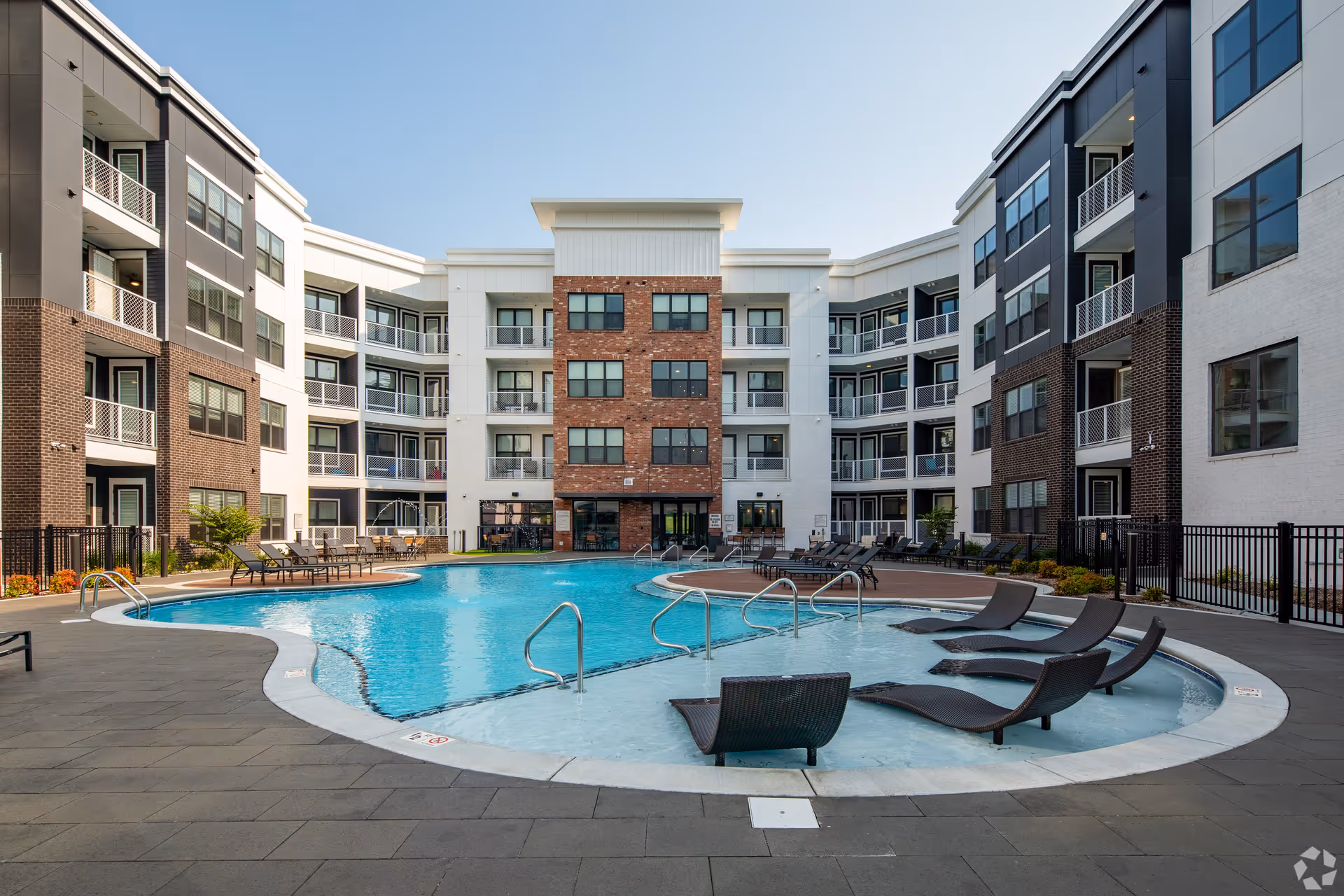 Modern four-story apartment building surrounding a courtyard swimming pool with lounge chairs.