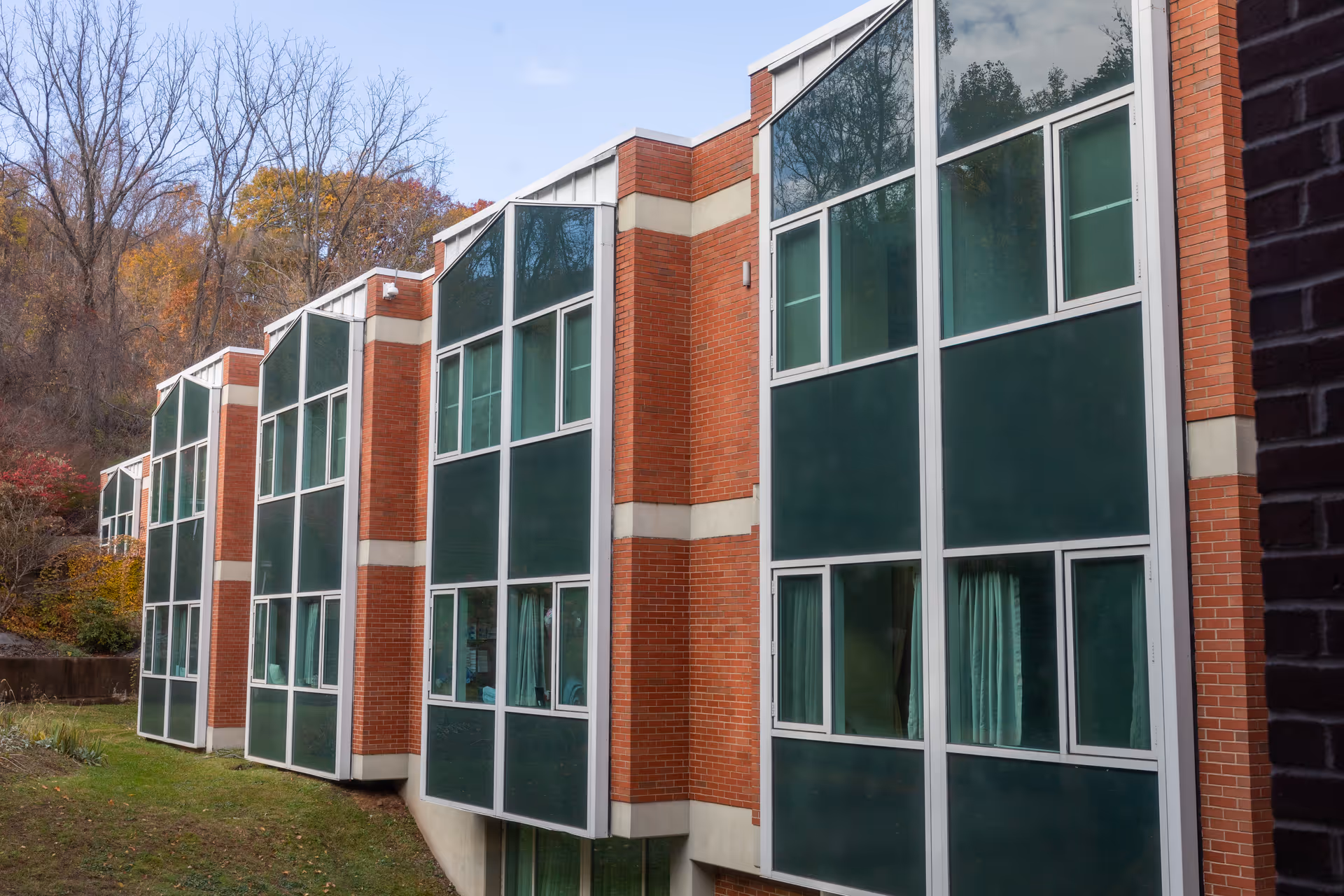 Exterior view of a multi-story brick building with large green and white framed windows, surrounded by trees with autumn foliage.