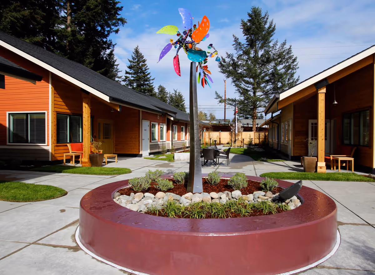 Courtyard of Cottages of University Place with a central circular planter featuring a colorful wind sculpture, surrounded by single-story cottage buildings and outdoor seating.
