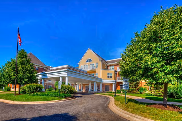 Sunlit senior living facility entrance with porte-cochère and landscaped grounds.