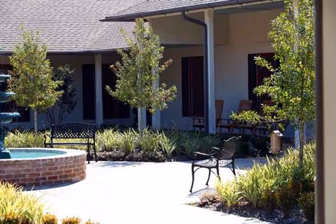 Outdoor courtyard at Camelot Brookside with a circular brick fountain, benches, and greenery.