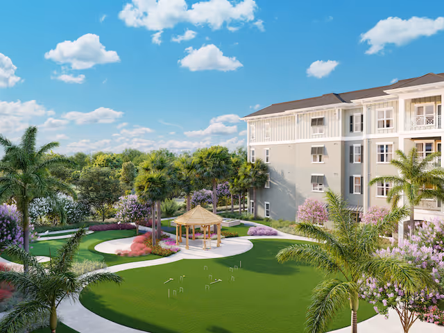 Outdoor garden area at Sonata Lake Mary featuring a green lawn with a small wooden gazebo in the center, surrounded by palm trees and flowering bushes. A multi-story residential building is visible on the right side under a blue sky with scattered clouds.