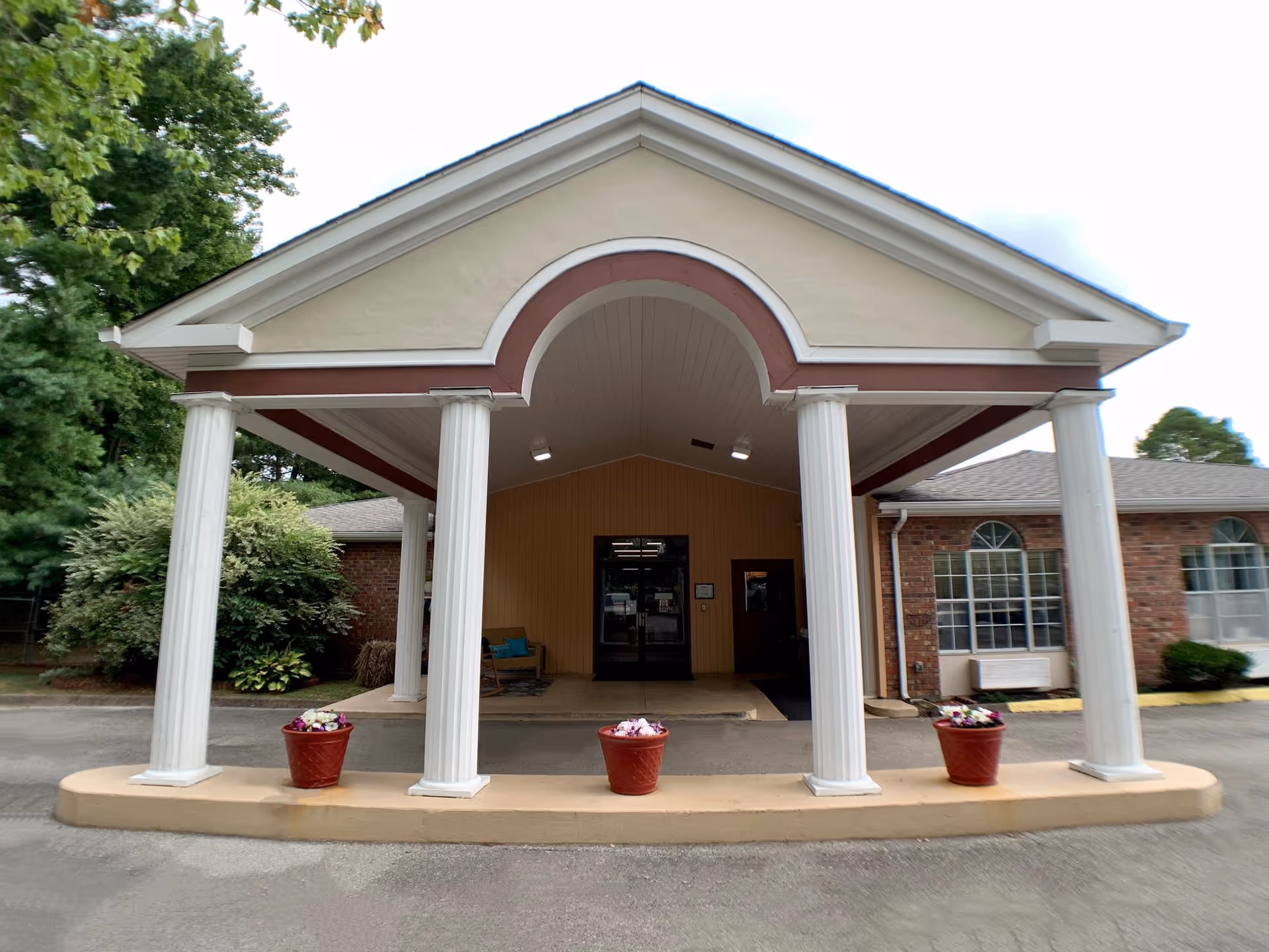 Front entrance of a brick building featuring a covered portico with four white columns and three flower pots.