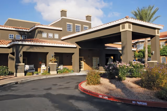 Exterior view of Brookdale Chandler Regional senior living facility showing the entrance with a covered drop-off area, landscaped bushes, and a clear blue sky.