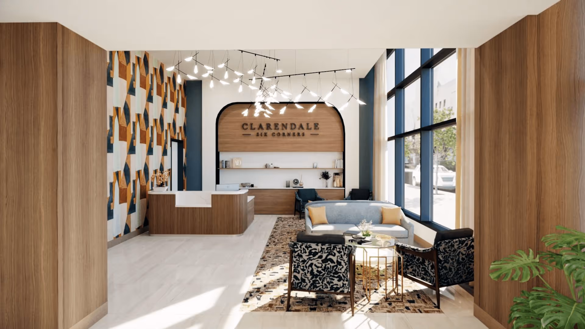 A modern and stylish lobby area of Clarendale Six Corners featuring a wooden reception desk, geometric patterned wall, contemporary light fixtures, large windows letting in natural light, a seating area with a gray sofa, two patterned armchairs, a small round table, and a decorative plant.