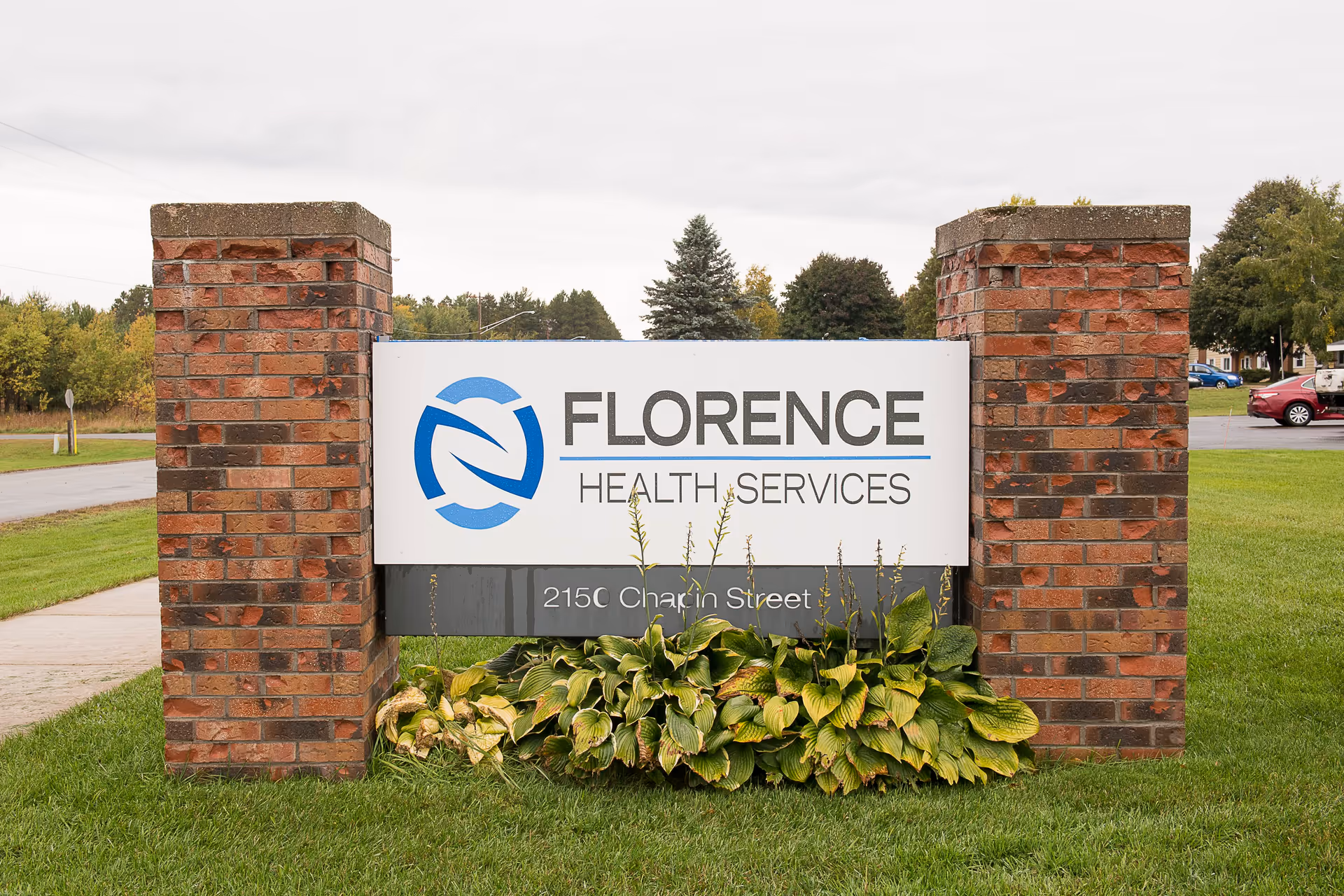 Brick entrance sign for Florence Health Services with logo and plants in front on a grassy lawn.