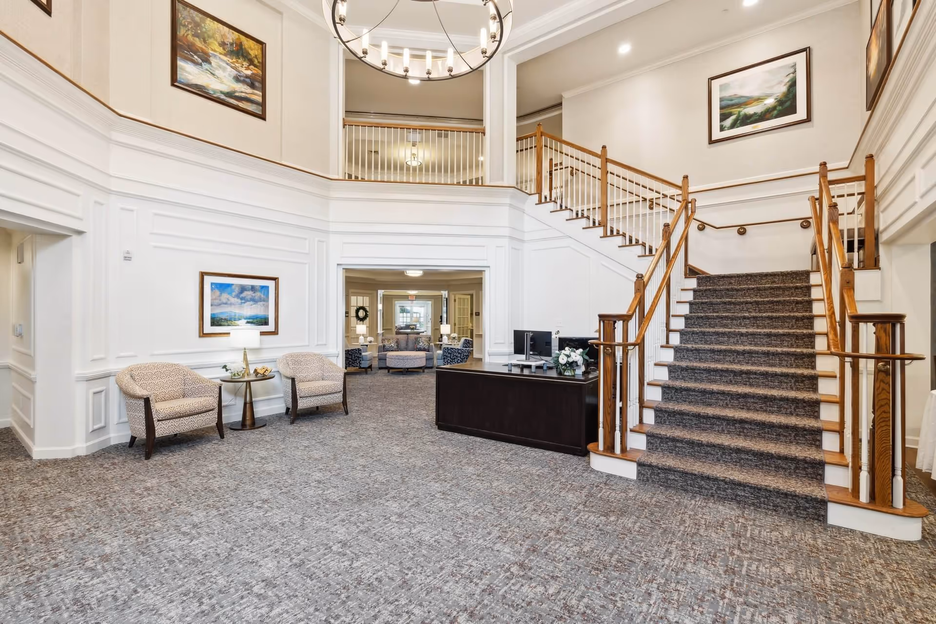 Spacious two-story lobby with a carpeted staircase, reception desk, seating area, and chandelier.