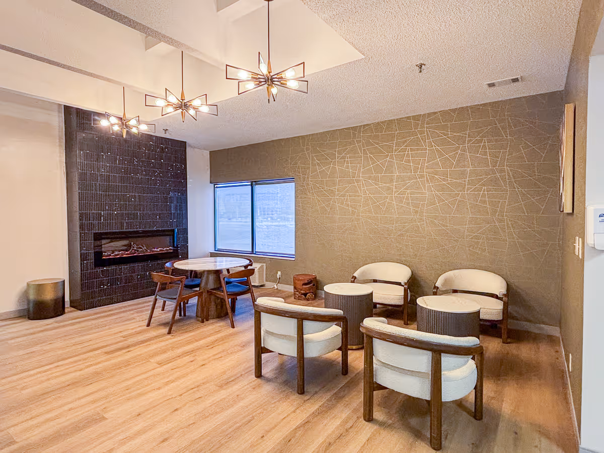 A modern communal lounge area in a senior living facility featuring a fireplace, seating, and large windows.