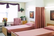 Two twin beds with pink linens in a shared senior living bedroom.