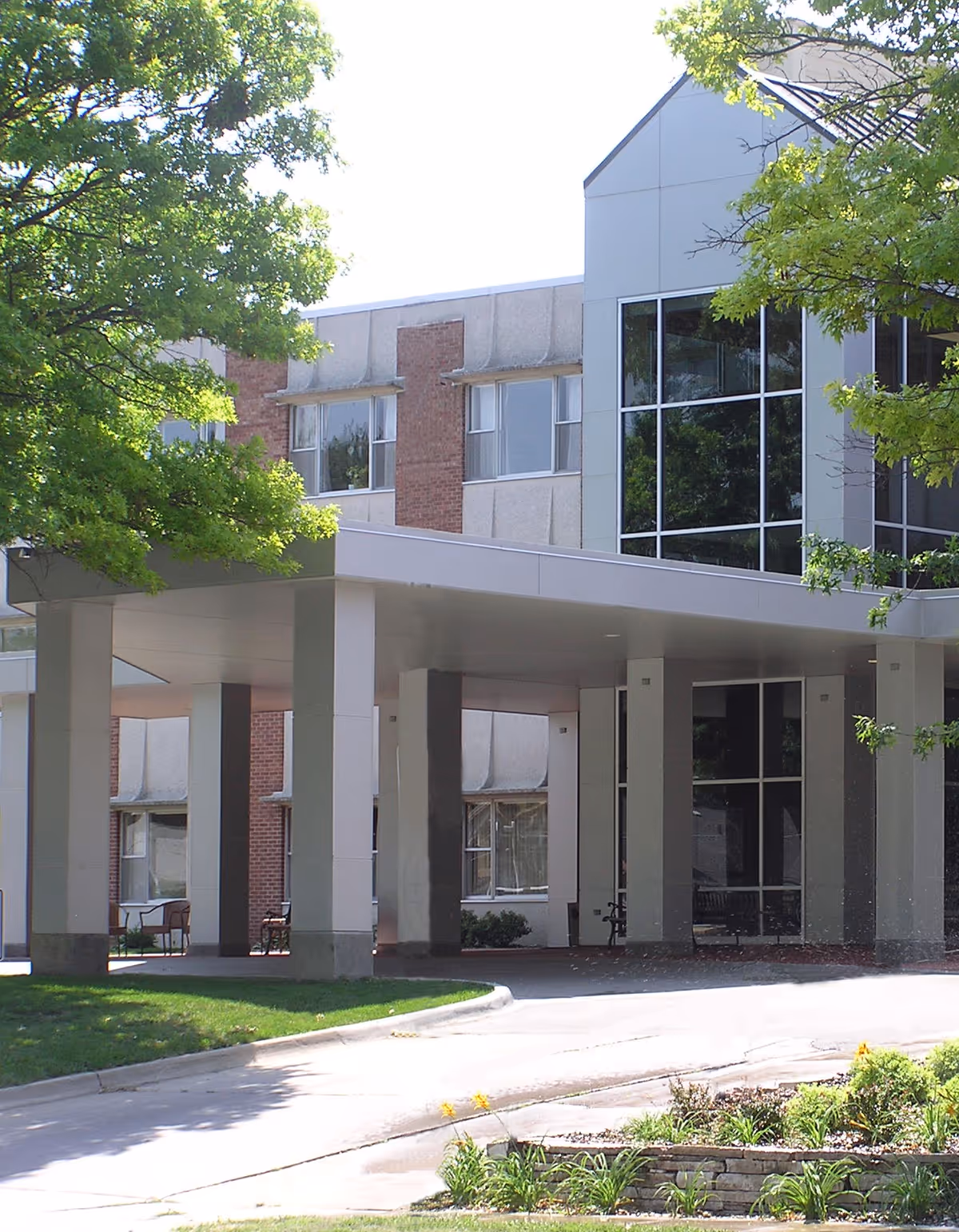 Covered entrance and porte-cochère of the Calvin Community building with columns, large windows, and surrounding trees.