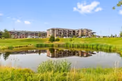 A multi-story senior living building reflected in a pond with grassy banks and a blue sky.