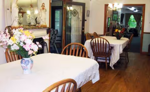 Interior dining room at Sacred Heart Adult Care Home with white tablecloth tables and flowers.