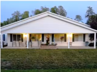 Front view of a single-story residential building with a covered porch, illuminated exterior lights, and a lawn.