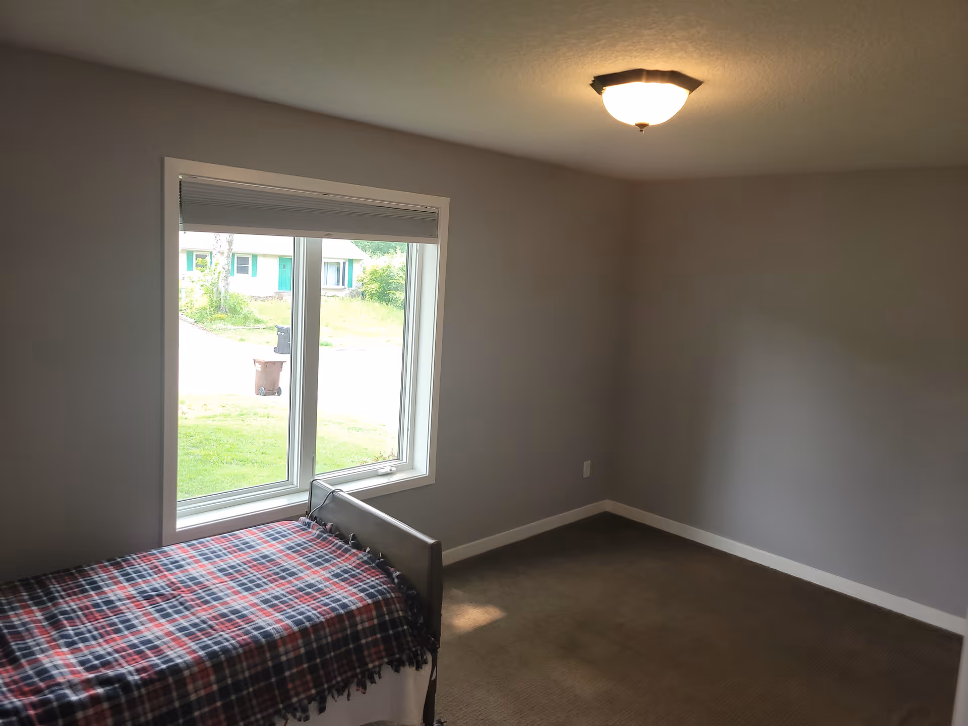Small sparsely furnished bedroom with a single bed by a large window and neutral gray walls.