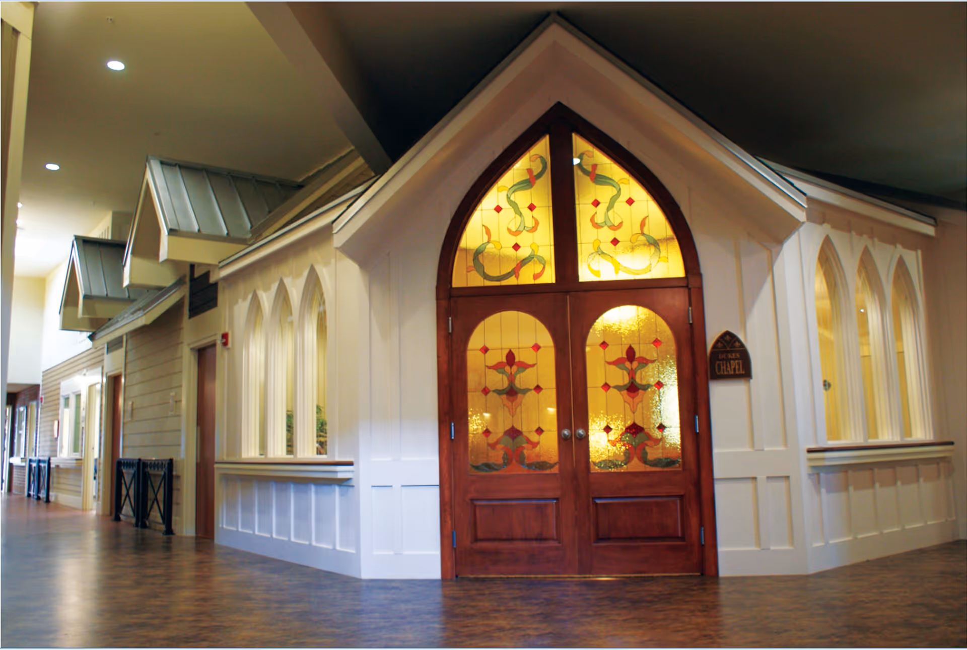 A bright interior hallway featuring a chapel-like room with arched stained-glass double doors and windows.