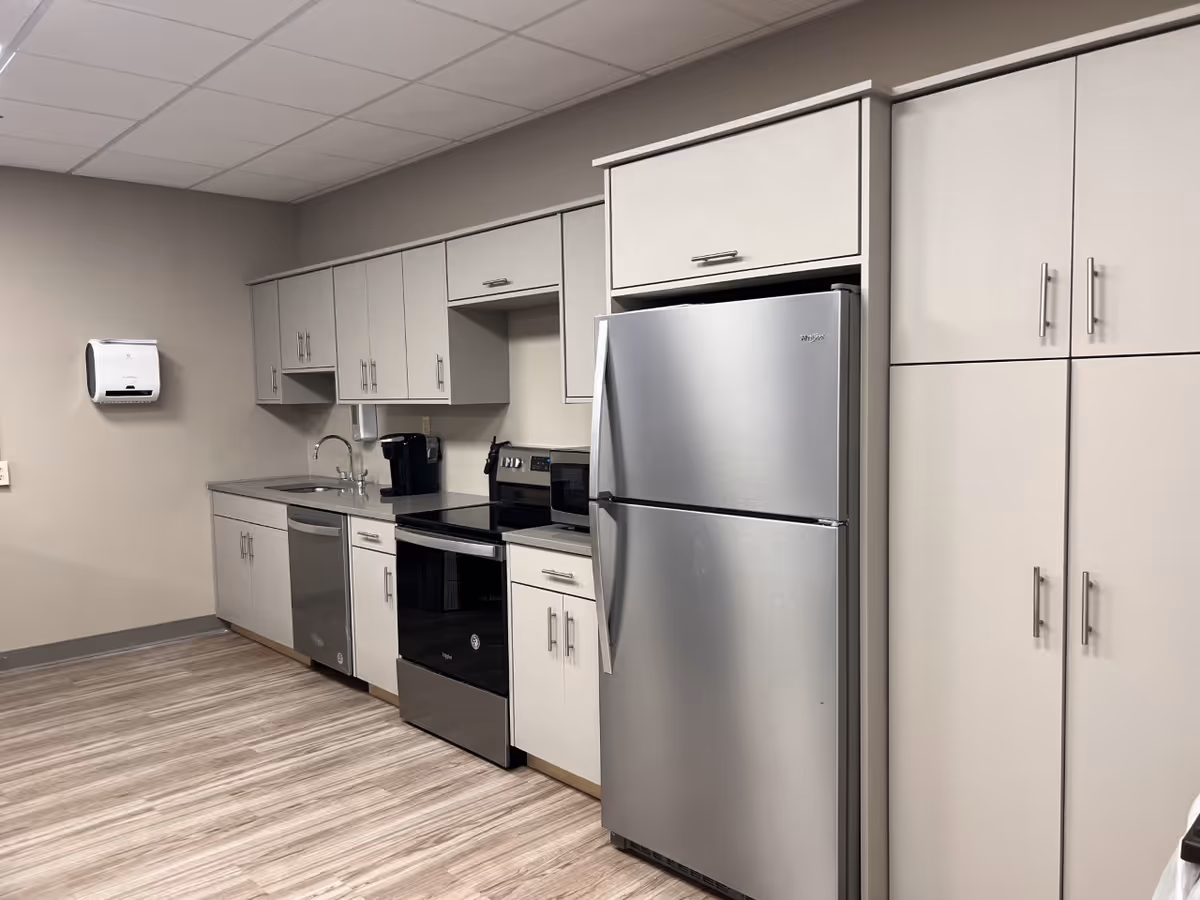 Small kitchen area with stainless steel refrigerator, stove, dishwasher, sink, cabinetry, and a coffee maker.