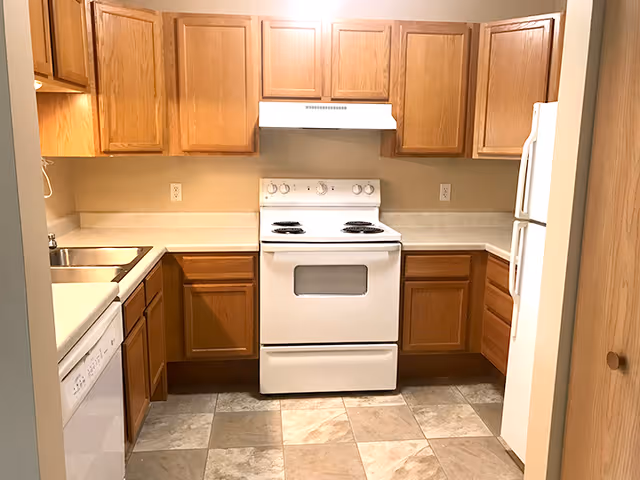 Small kitchen with oak cabinets, a white electric stove and hood, refrigerator, dishwasher, double sink, and tiled floor.