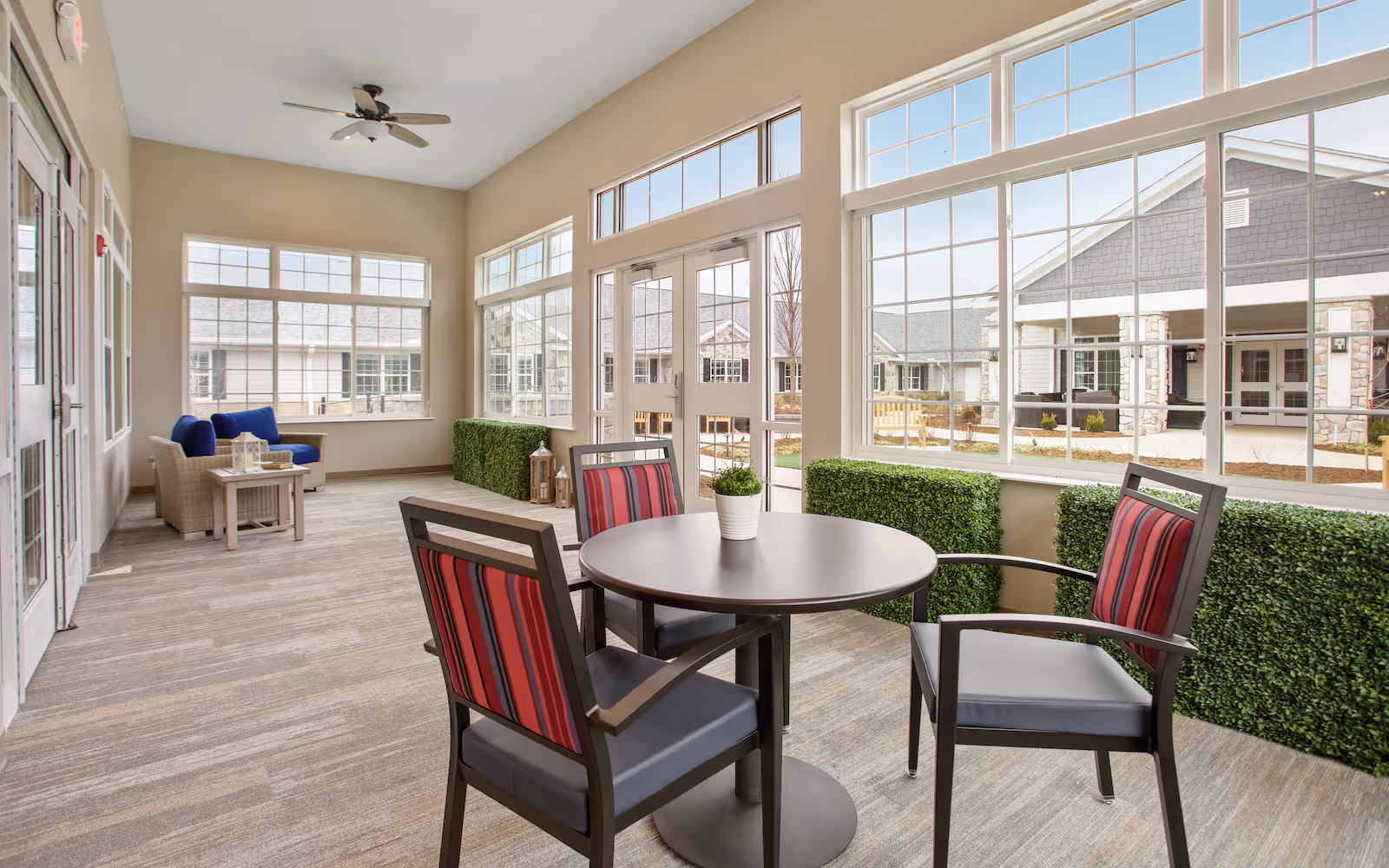 Sunlit common room with a round table and four chairs, lounge seating, and large windows overlooking the courtyard.