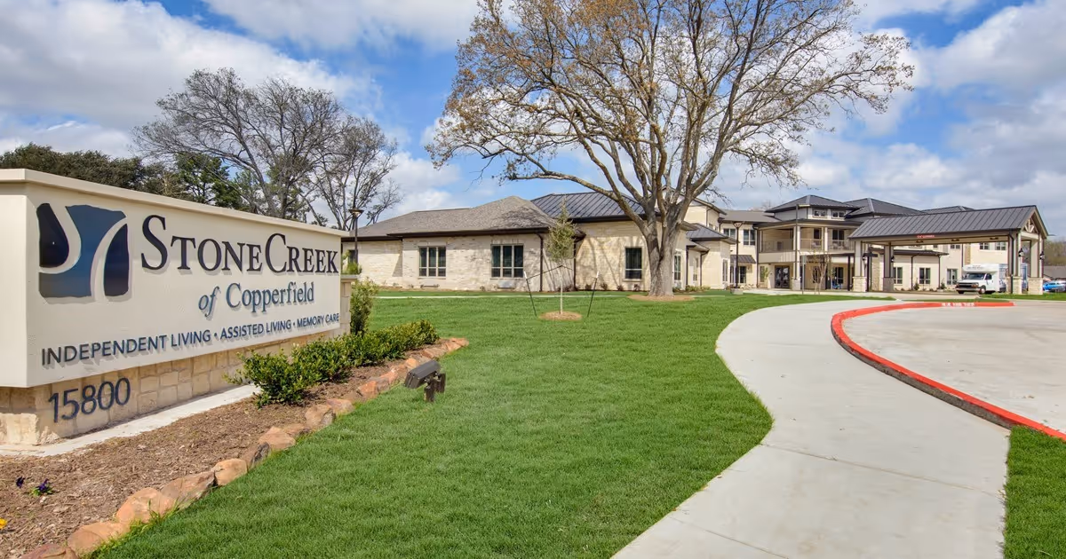 StoneCreek of Copperfield senior living building front with a large entrance sign, lawn, and curved driveway.