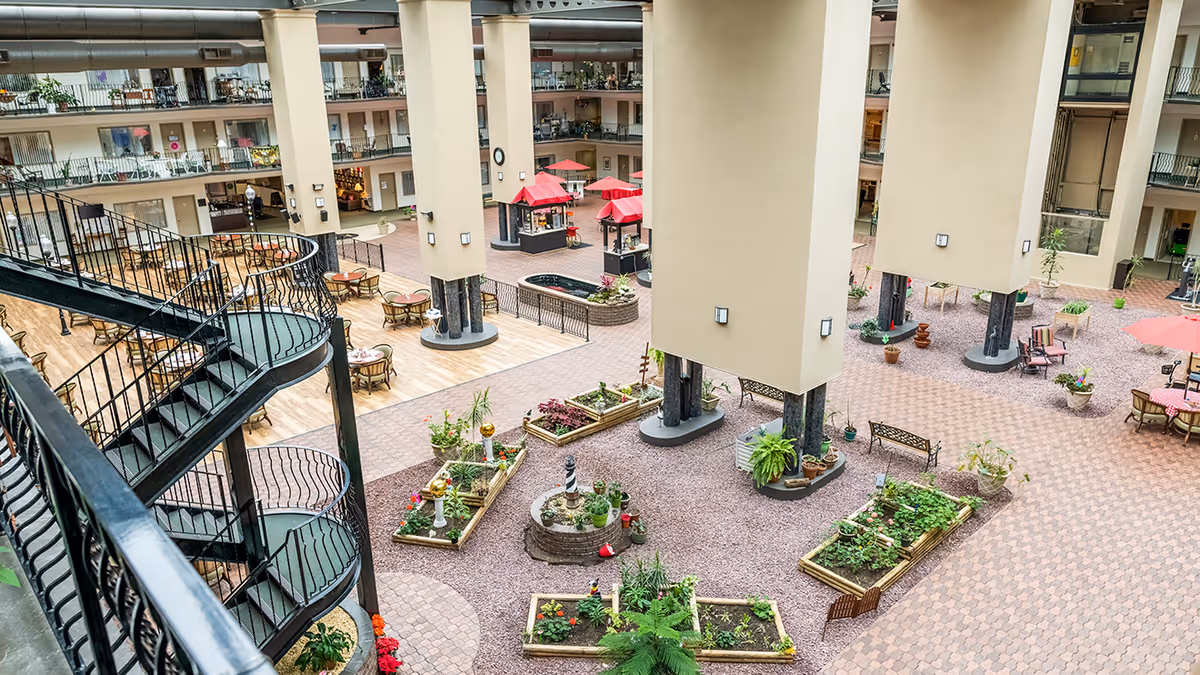 Indoor multi-story atrium with central garden beds, seating and tables, and a spiral staircase overlooking the courtyard.