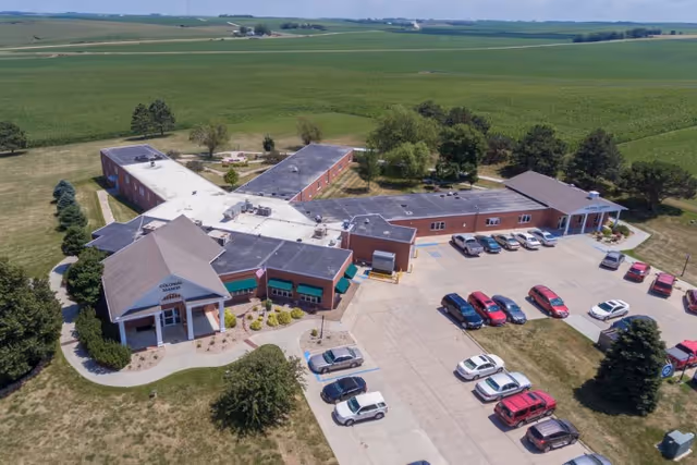Aerial view of Colonial Manor Of Randolph senior living facility with parking lot surrounded by farmland.