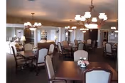 Communal dining room with multiple tables and upholstered chairs, chandeliers, and floral centerpieces.