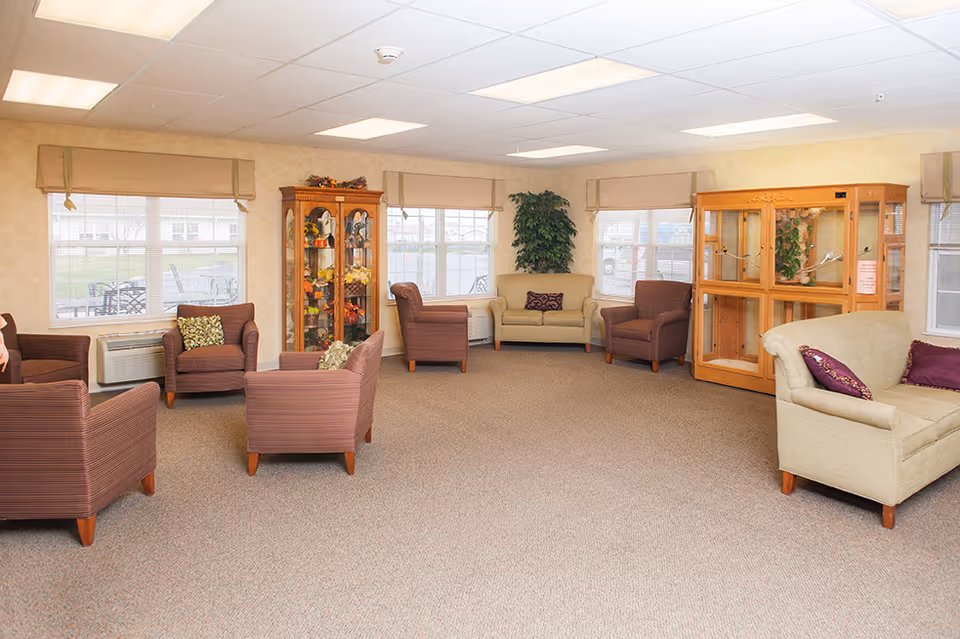 Common lounge with armchairs, sofas, display cabinets, and large windows in a retirement community.