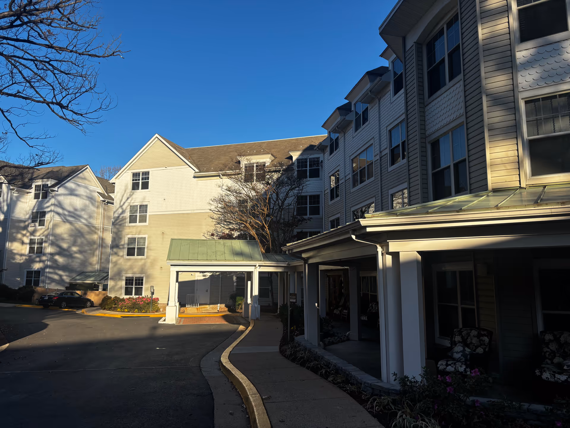 Exterior front entrance of a multi-story senior living building with a covered driveway under a clear blue sky.