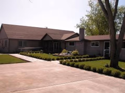 A single-story senior living facility exterior with a concrete driveway and landscaped front yard.