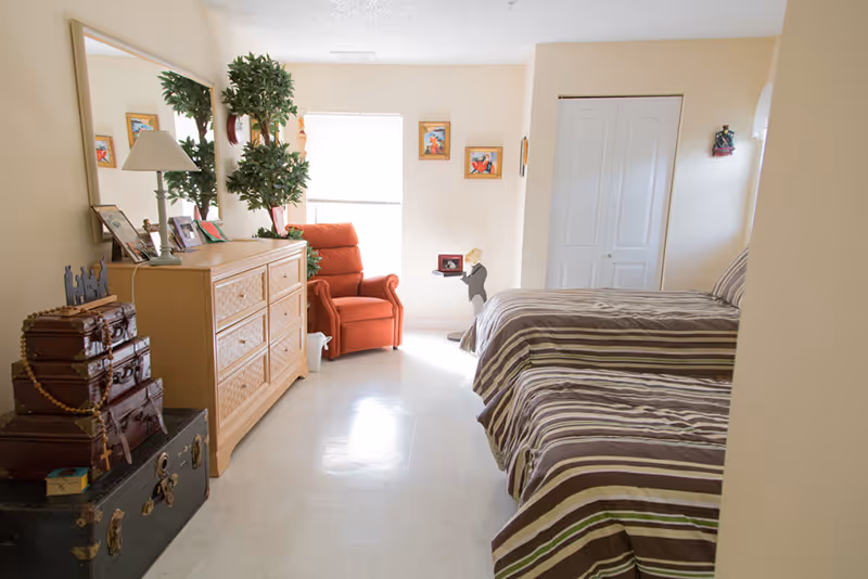 Two twin beds in a cozy senior living bedroom with dresser and red armchair.
