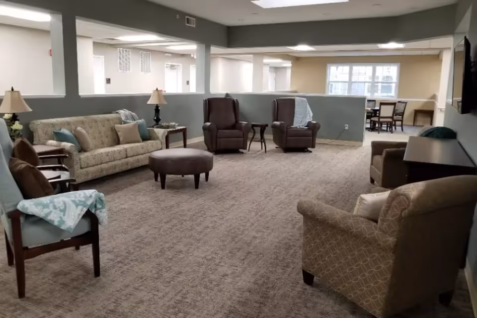 Spacious interior lounge with sofas, armchairs, an ottoman, side tables and lamps arranged on carpeted floor.