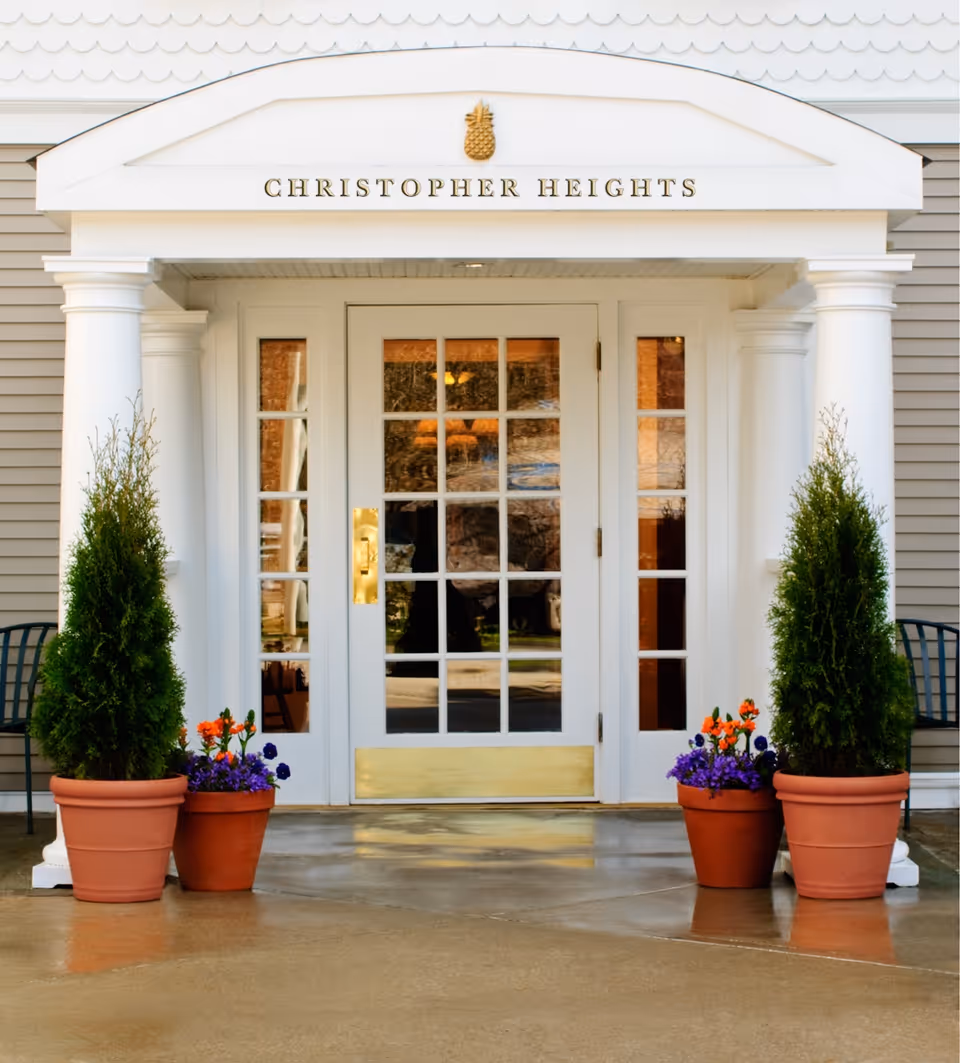 The main entrance to Christopher Heights featuring white glass-paneled double doors flanked by columns and potted plants with the facility name above.