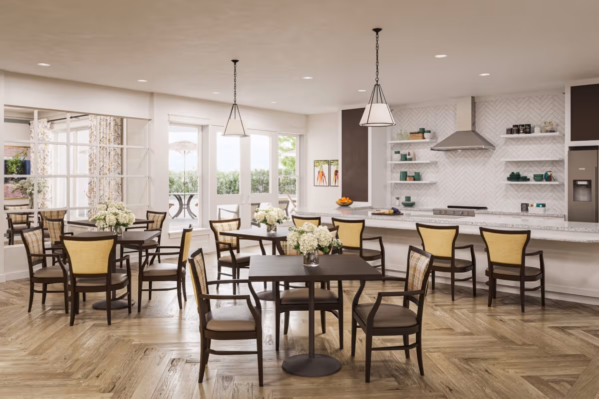Communal dining area with several tables and chairs, floral centerpieces, and a long kitchen counter with barstools.