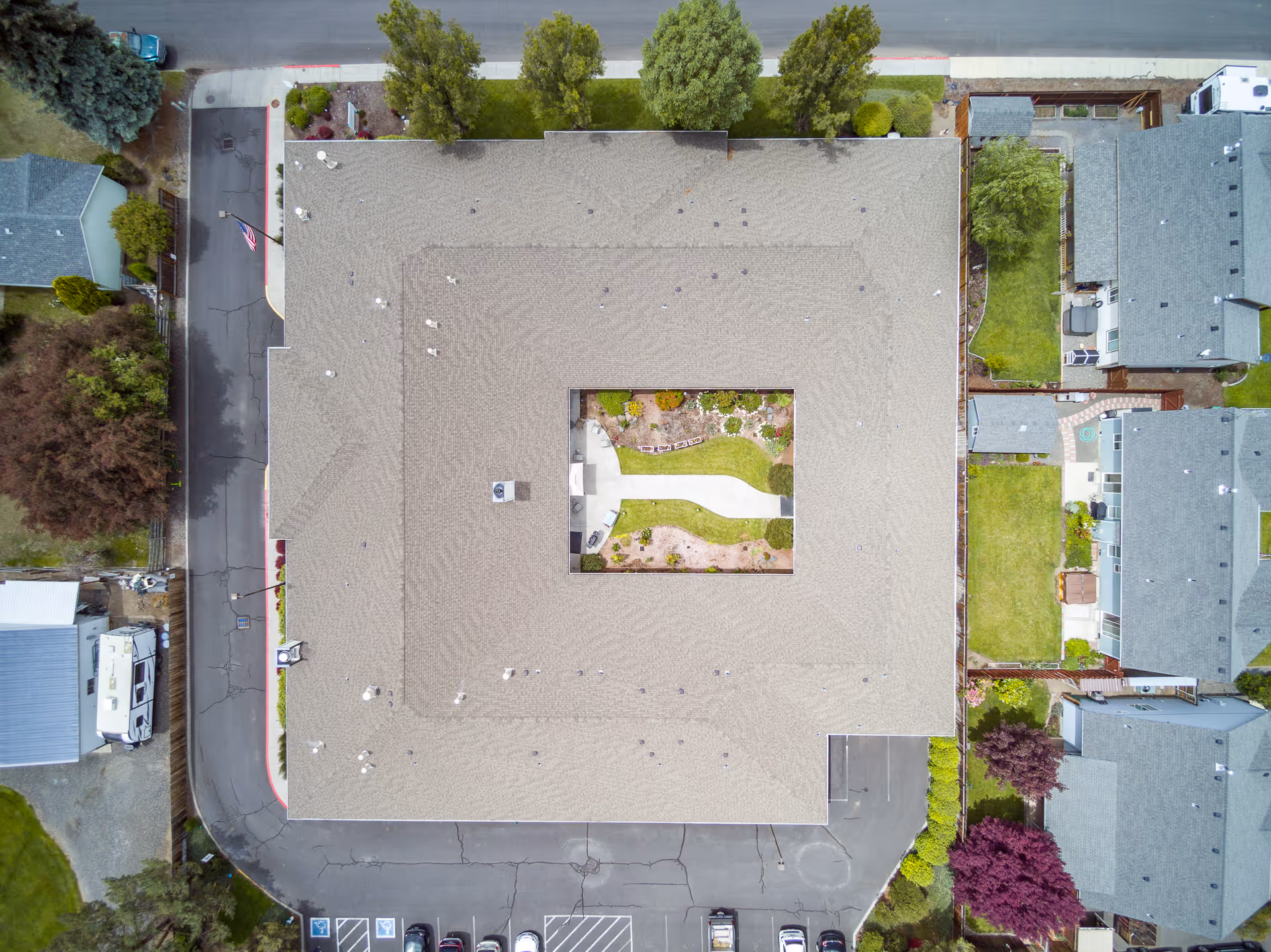 Aerial top-down view of a large rectangular building with a central courtyard, surrounding parking lot and neighboring houses.