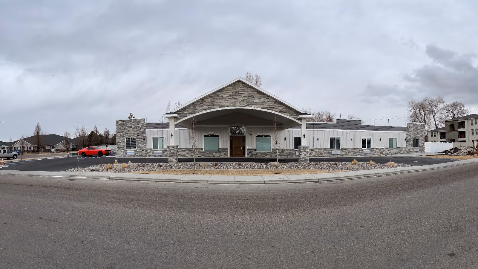 Single-story residential care building with a covered arched entrance and stone facade under an overcast sky