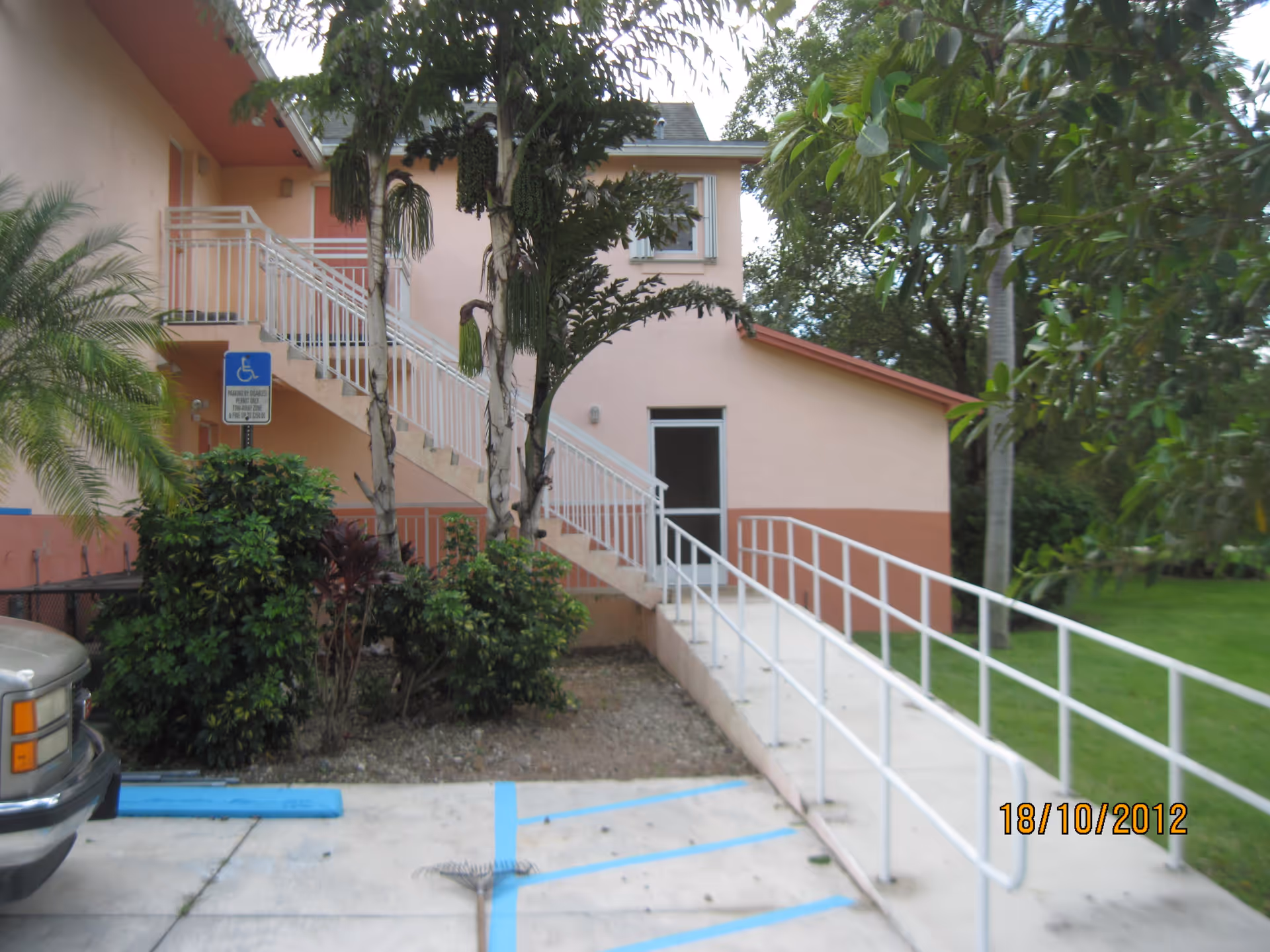 Exterior front of a pink building with a wheelchair ramp and stairs, palm trees, and a handicapped parking spot.