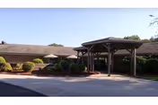 Single-story facility entrance with a covered drive-through canopy, landscaped shrubs, and a paved driveway.