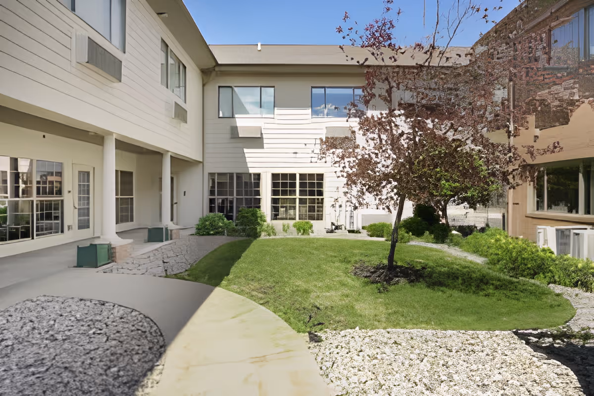 Small grassy courtyard with a single tree surrounded by a two-story building.