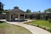 Courtyard with a central gazebo, paved walkway, lawn and surrounding single-story brick building under a clear blue sky.