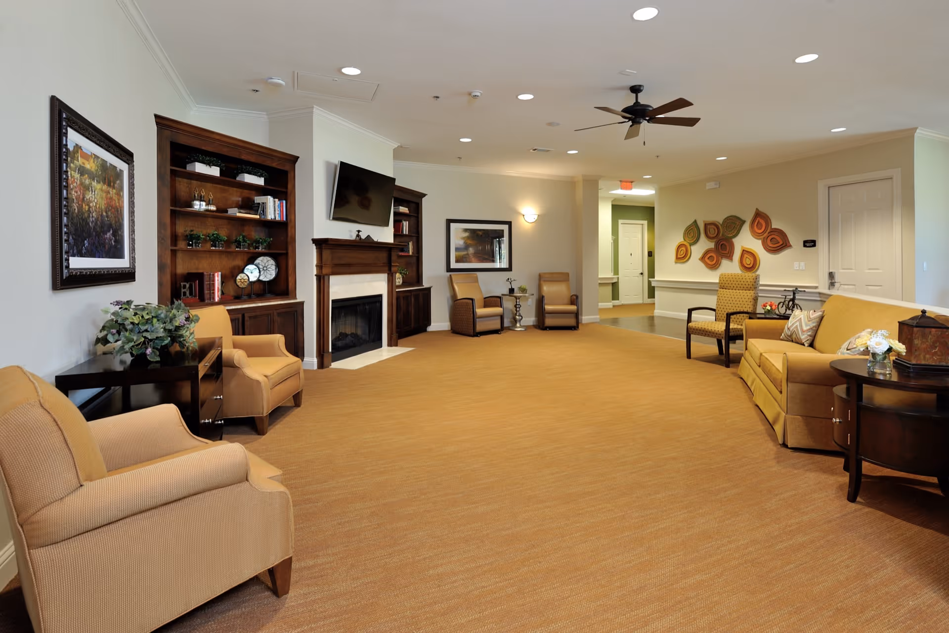 Spacious senior living lounge with seating, fireplace, built-in shelves and a wall-mounted TV.