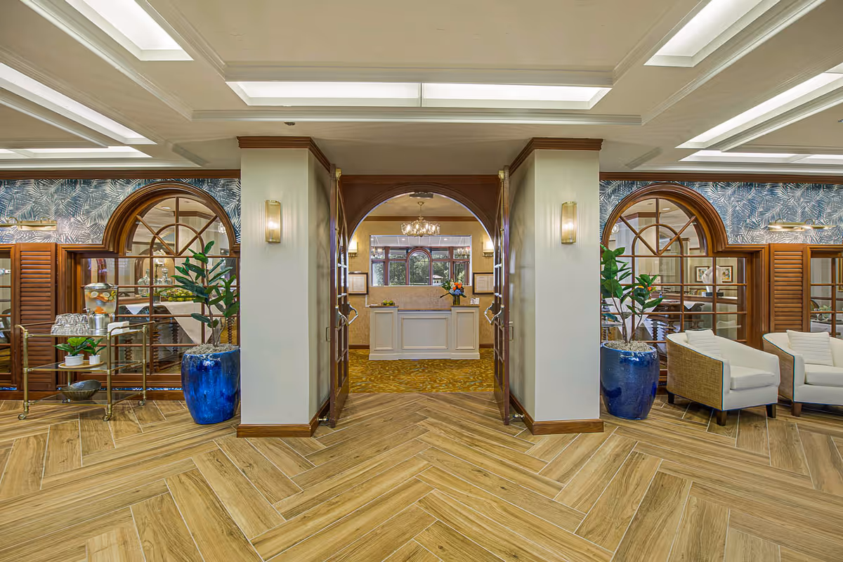 Bright, elegant reception lobby with herringbone wood floors, a central front desk, arched doorways, potted plants and lounge seating.