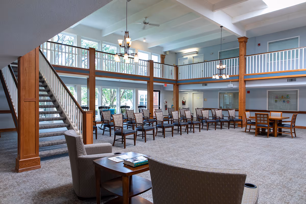 Spacious two-story common lounge with rows of chairs, a seating area and a staircase next to large windows.